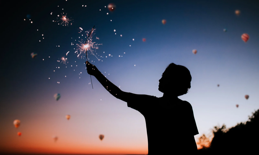 A boy with a sparkler creating a silhouette against the sky.