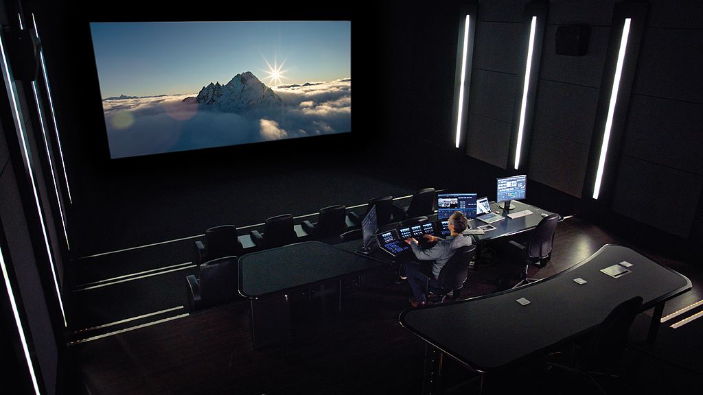 A man is sitting at a desk in front of a large screen, working as a cinematographer.