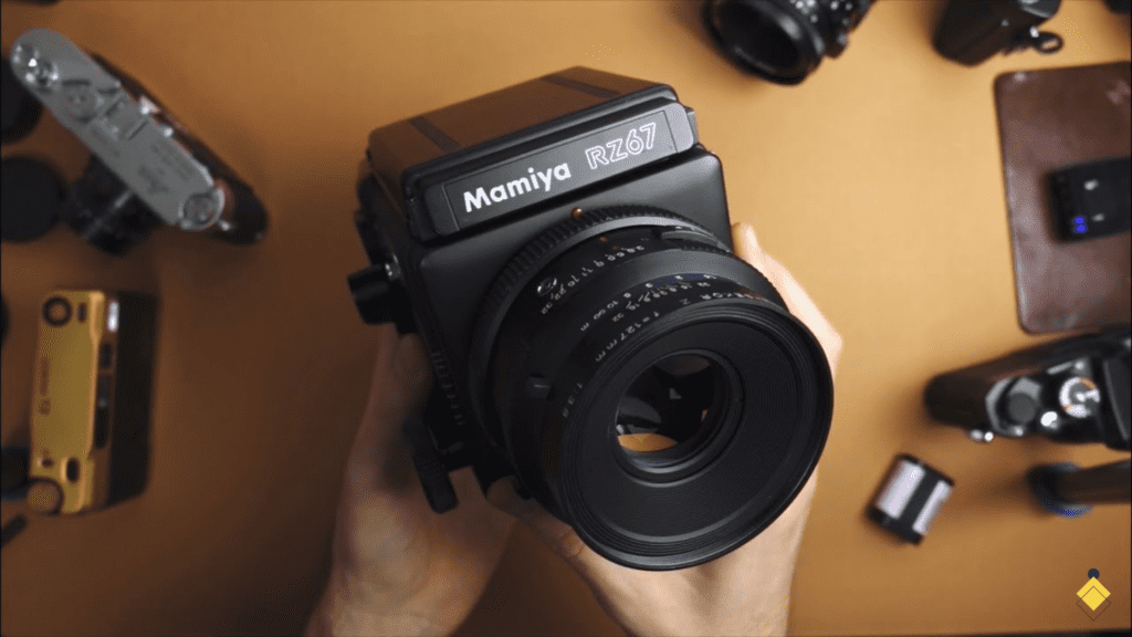 A person holding a Mamiya RZ67 camera with other items around it.