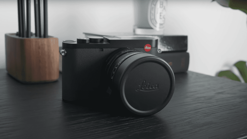 A Leica Q3 camera sitting on a table next to a plant.