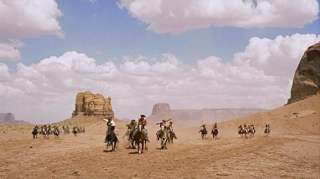 Wide shot of cowboys riding horses in the desert.