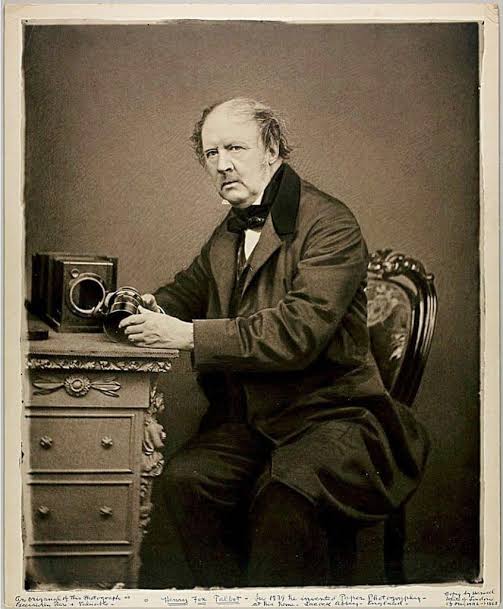 An old photograph of a man holding a camera from when the camera was invented.