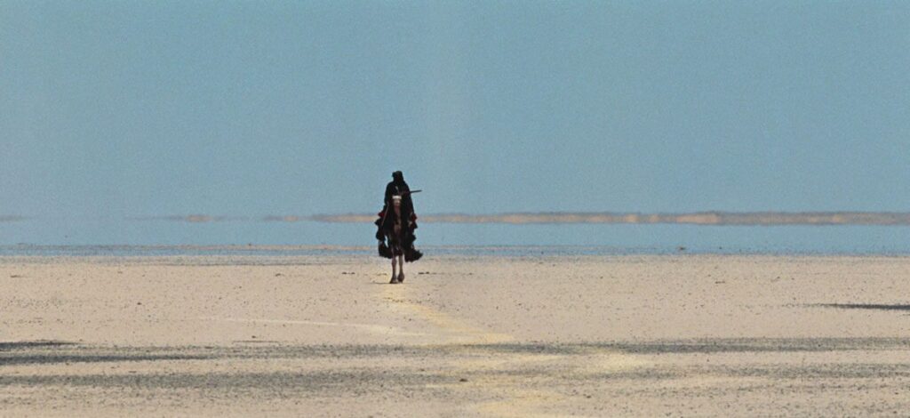 Wide shot of a man walking down a deserted road.
