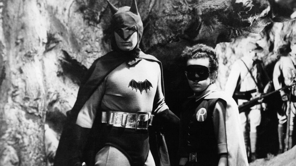 A black and white photo of Batman with a young boy, showcasing their iconic dynamic duo partnership.