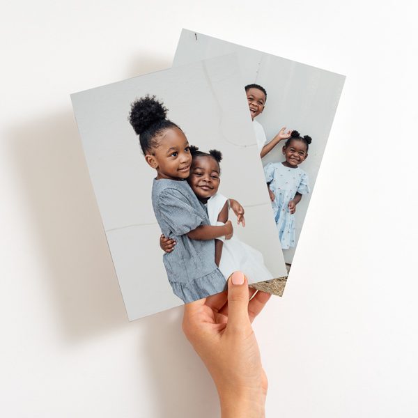 A hand holding two photo cards with a black child in the middle, captured in a 4x6 size.