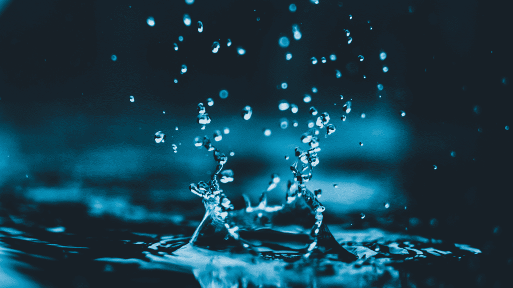 Water splashing dynamically with droplets suspended in the air, captured using precise photography exposure triangle settings, against a dark blue background.