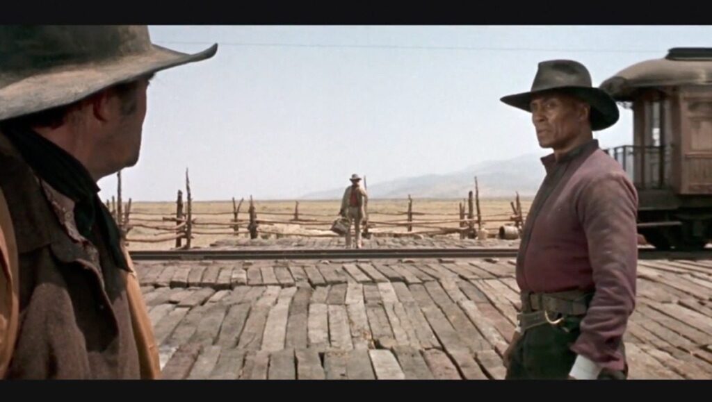 Two cowboys face each other in a tense standoff on a wooden platform, with a train and vast open landscape captured using optimal settings of the photography exposure triangle in the background.