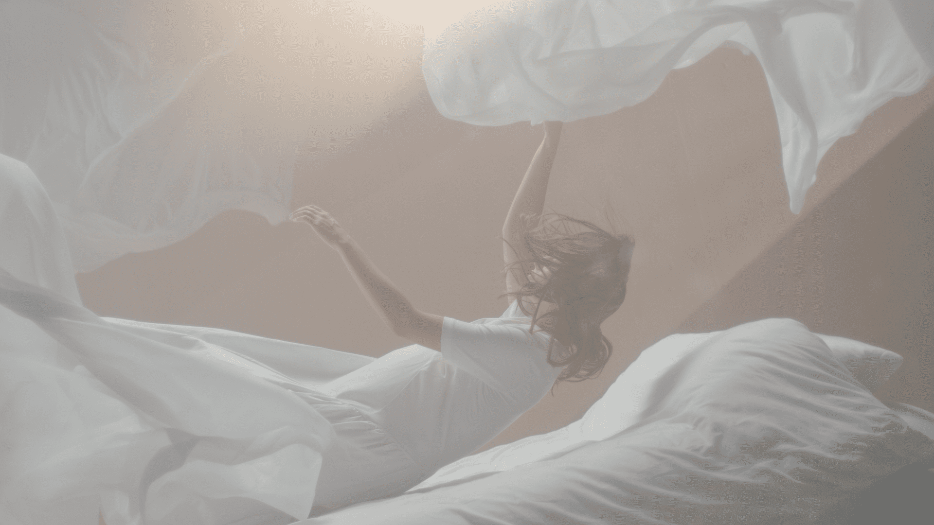 A woman in a white dress appears to float among swirling white sheets in a soft-lit, dreamlike setting.