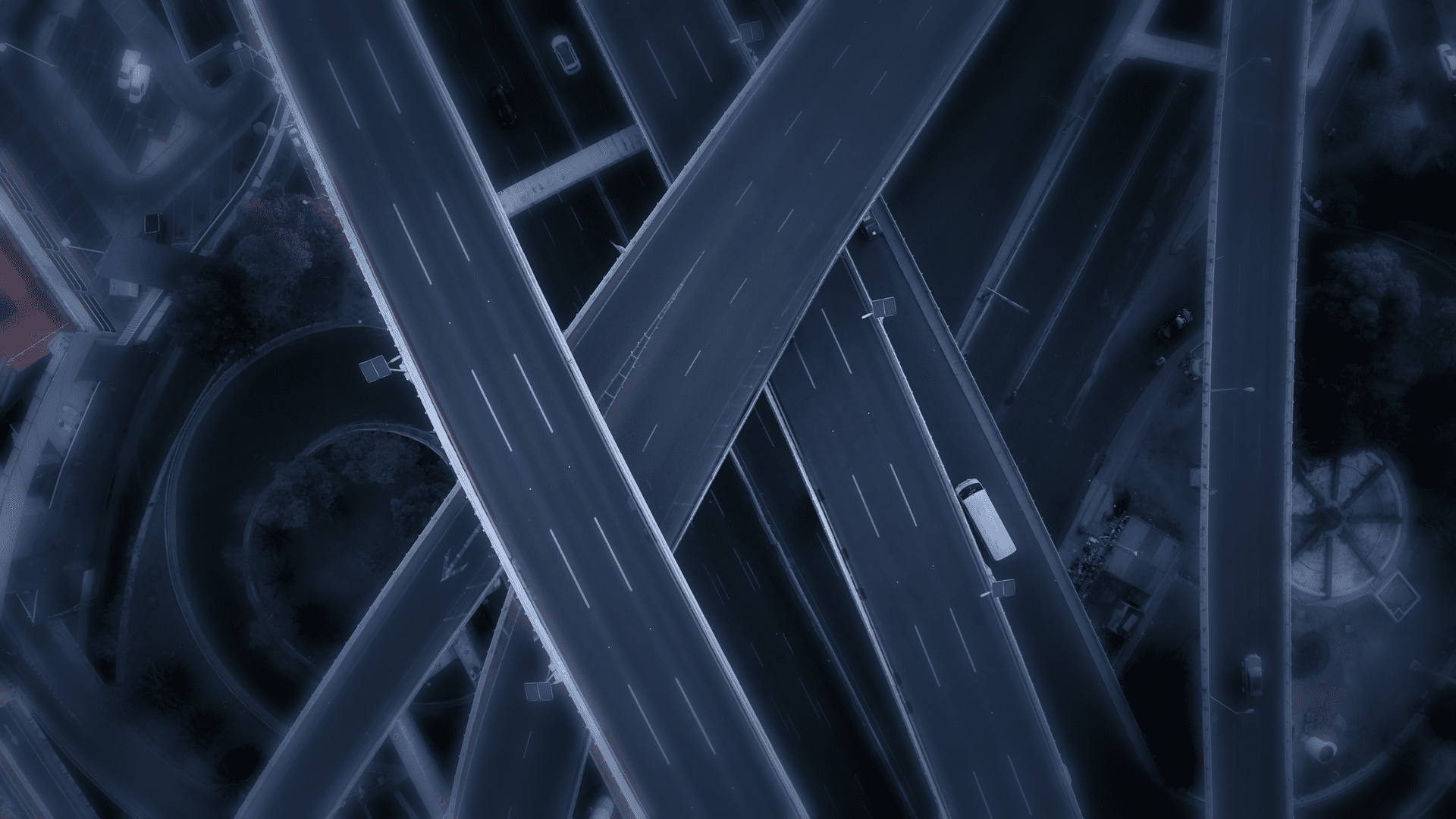 Aerial view of a complex highway interchange at night, with multiple overlapping roads and a few vehicles visible.