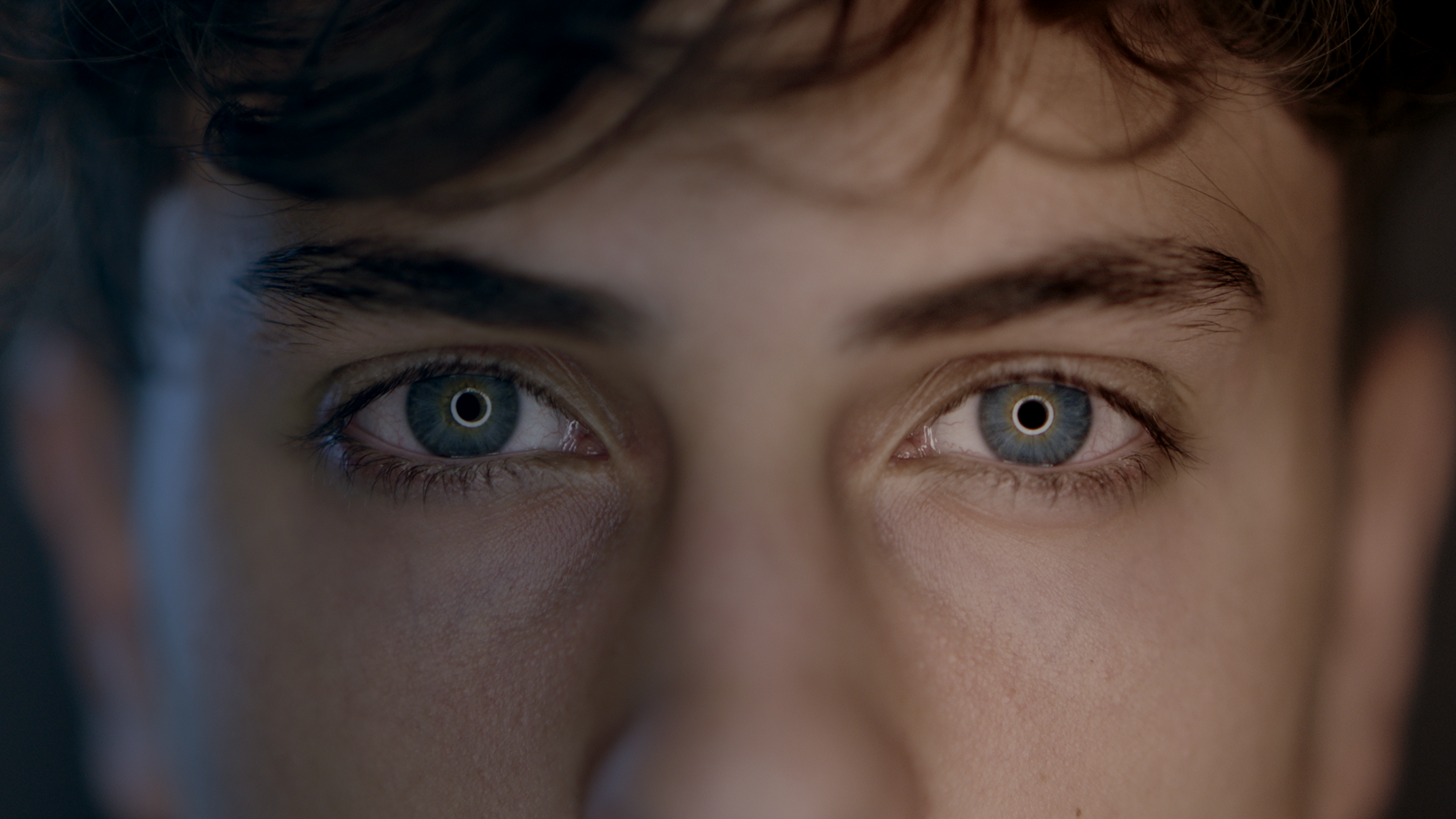 Close-up of a person's eyes with intense gaze, highlighting blue irises and long eyelashes.