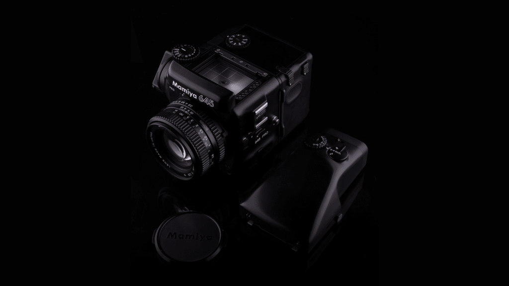 The Mamiya 645 medium format camera elegantly stands against a dark background, featuring a detachable film back and lens cap.