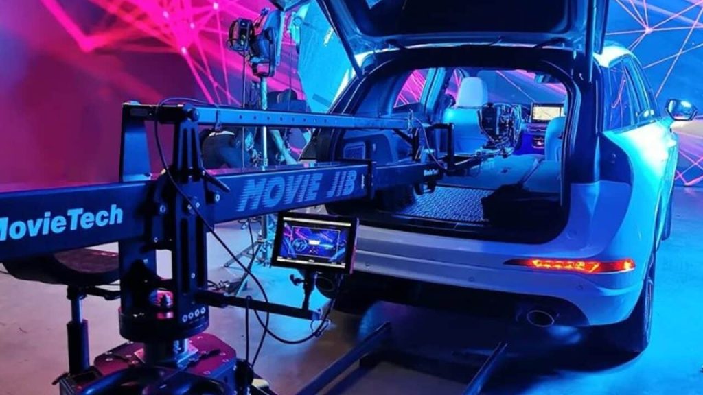 A film camera jib, expertly managed by the key grip, is positioned behind a white SUV with its trunk open, set in a studio with vibrant lighting.