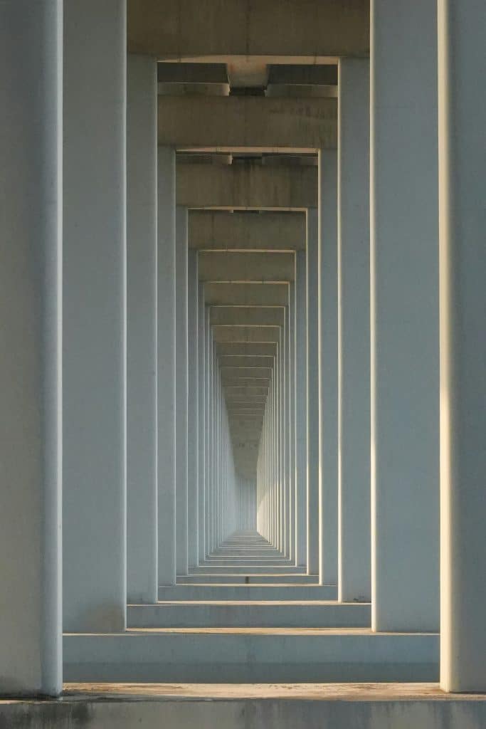 A symmetrical view of concrete beams forms a tunnel-like corridor under a bridge, with diminishing perspective and soft lighting, perfectly capturing the essence of landscape architecture.