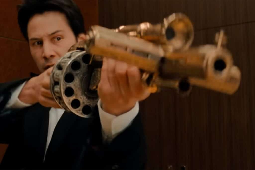 A person in a suit is aiming an intricately designed, multi-barreled gun indoors, reminiscent of iconic scenes featuring guns in movies.