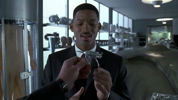 In a sleek laboratory, a man in a suit attentively inspects a futuristic gun, akin to those often seen in the latest guns in movies, handed to him by another individual.