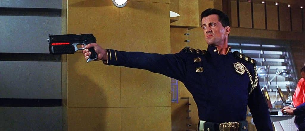 A person in a navy blue uniform aims a futuristic handgun, reminiscent of those iconic guns in movies, in a room with yellow walls and various equipment.