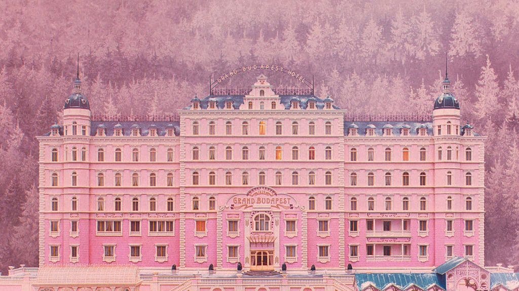 A grand, symmetrical pink hotel with classic architecture, labeled "Grand Budapest Hotel," set against a backdrop of a misty forest, showcases the whimsical charm of a Wes Anderson color palette.