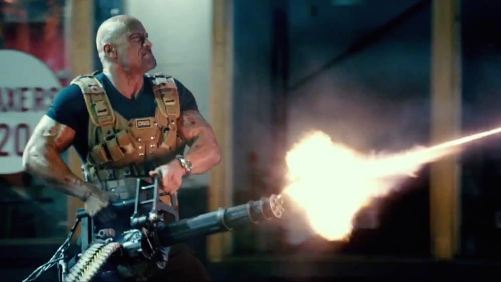 A muscular man in tactical gear is firing a large machine gun, its barrel aflame, evoking the intense action found in Guns in Movies, set against an urban nighttime backdrop.